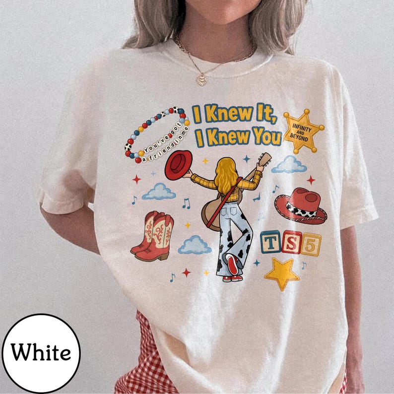 May include: A white t-shirt featuring a graphic print of a person with long blonde hair playing a guitar, surrounded by cowboy boots, a red hat, a beaded bracelet with the text You've got a friend in me, a yellow star, and the text I Knew It, I Knew You.