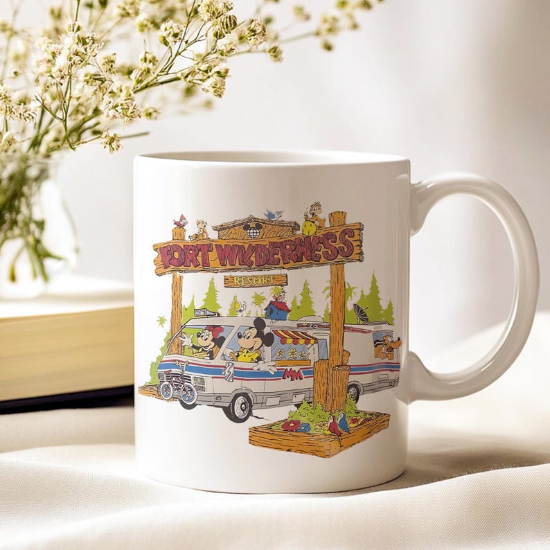 K&ouml;nnte beinhalten: Wei&szlig;e Keramiktasse mit einer farbenfrohen Illustration von Mickey und Minnie Mouse in einem Van mit dem Text "Fort Wilderness Resort". Die Tasse hat einen gebogenen Henkel. Der Hintergrund ist weich und neutral.