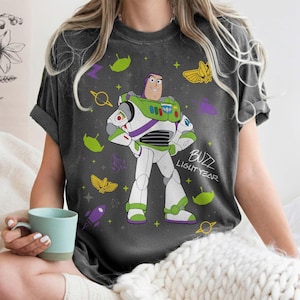 May include: Dark gray t-shirt featuring a cartoon illustration of Buzz Lightyear from Toy Story. The design includes Buzz in his spacesuit, surrounded by space-themed graphics and the text "Buzz Lightyear".