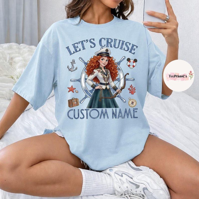 Pu&ograve; includere: T-shirt azzurra con la scritta "LET'S CRUISE" e "CUSTOM NAME". La grafica presenta un personaggio dei cartoni animati in uniforme da capitano, un timone e elementi nautici come un'ancora e una stella marina.