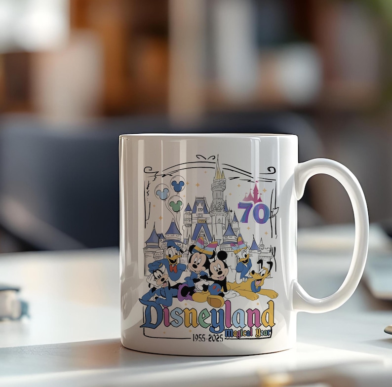 May include: White ceramic mug featuring a colorful Disneyland design. The design includes Mickey Mouse, Donald Duck, and other characters in front of a castle, with the text "Disneyland" and "70 Magical Year".