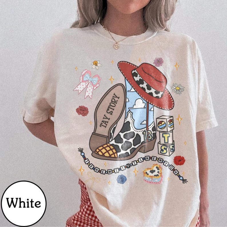 May include: A white t-shirt featuring a graphic print of a cowboy boot with cow print patterns, a red hat, building blocks with the letters T, S, and the number 13, a pink bow, and a beaded string with the text I KNEW IT I KNEW YOU.