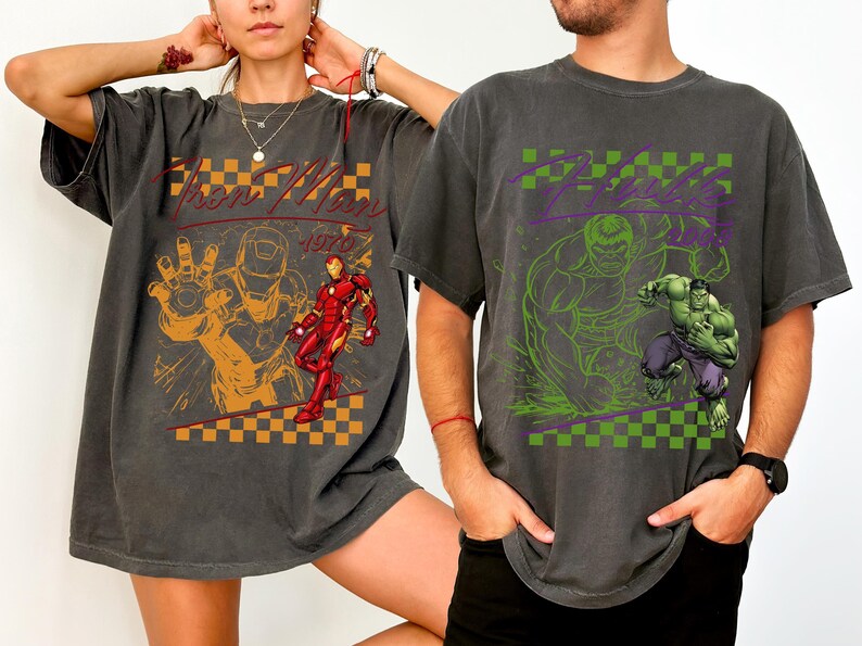 May include: Two charcoal gray t-shirts featuring comic book characters. One shirt displays "Iron Man 1970" with an orange and red graphic. The other shirt features "Hulk" with a green and purple graphic.