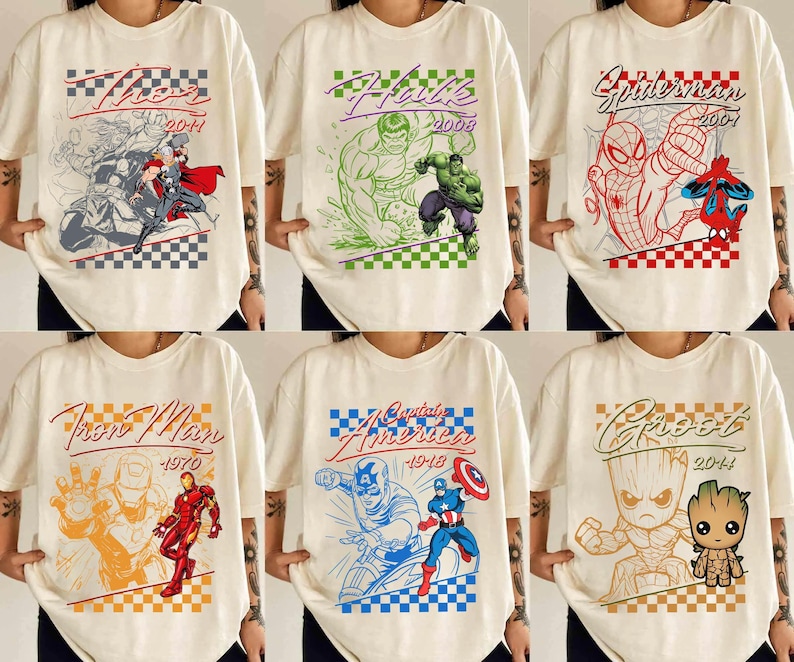 May include: Cream-colored t-shirts featuring various Marvel comic book characters. Designs include Thor, Hulk, Spider-Man, Iron Man, Captain America, and Groot, each with their name and year. The graphics are in a comic book style with a checkered pattern.