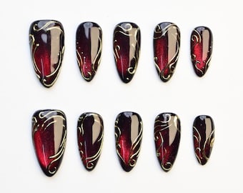 Acrylnagels in amandelrood en zwart, gotische nagels in wijnrood met gouden lijnen, luxe glanzende nagels met donkere aura, handgemaakte gelnagels met kleurverloop in vampierstijl.
