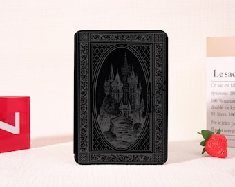 Könnte beinhalten: Schwarzes Notizbuch mit geprägtem Design, das eine gotische Schloss-Szene in einem ovalen Rahmen zeigt. Der Einband ist mit Zierornamenten und einer strukturierten Oberfläche verziert, was auf ein Vintage- oder Fantasy-Thema hindeutet.