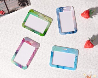 May include: Four ID badge holders with colorful, abstract designs. Each holder has a rectangular window for an ID card. The holders are in shades of green, blue, and pink. Two red strawberries are also in the image.
