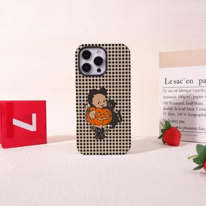 May include: A smartphone case featuring a beige and black gingham check pattern. The center displays a vintage-style illustration of a child wearing a pumpkin costume, accompanied by a black cat. The design includes small green leaf accents.