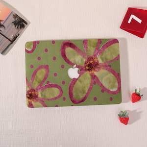 May include: A green laptop case with a floral design. The case features large, stylized flowers in shades of pink and yellow, with a white Apple logo cutout. The background is a light green with pink polka dots.