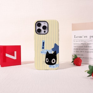 May include: A phone case with a cartoon cat design. The case has a yellow background with blue vertical lines. A black cat with large white eyes and a blue bow tie is featured, along with fish and an exclamation point.