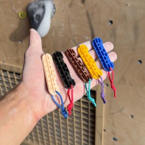 Puede incluir: Seis herramientas de entrenamiento de dedos de diferentes colores con un lazo en el extremo. Las herramientas están hechas de plástico y tienen una superficie texturizada. Los colores son beige, negro, marrón, amarillo, azul y morado.