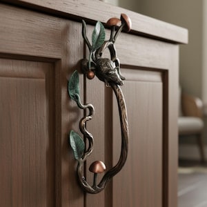 May include: A bronze cabinet pull with a forest-inspired design. The pull features a deer head, leaves, and mushrooms. The handle is a curved, branch-like design, adding a touch of nature-inspired elegance to the cabinet.