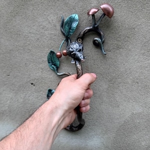 Könnte beinhalten: Dekorativer Türgriff aus Metall mit einem von der Natur inspirierten Design. Der Griff zeigt Blätter, Beeren und Pilzdetails. Der Griff wird in einer Hand gehalten, um seine Größe und Handwerkskunst hervorzuheben.