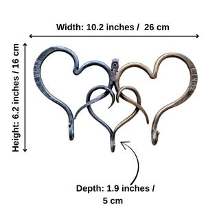 May include: A metal wall hook with a heart design. The hook is 10.2 inches wide, 6.2 inches high, and 1.9 inches deep. The design features three intertwined hearts in shades of gray and bronze. The names "LUCAS" and "LINDA" are inscribed on the hearts.