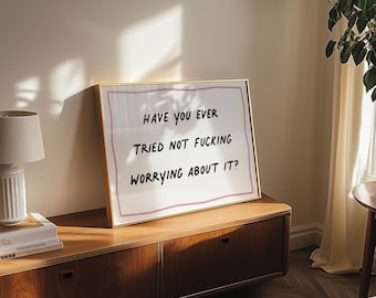 May include: A gold framed print with the text "Have you ever tried not fucking worrying about it?" on a white background. The print is sitting on a wooden dresser.