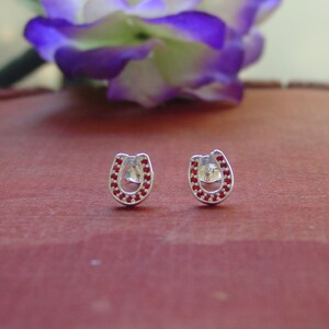 May include: A pair of silver horseshoe earrings with red cubic zirconia stones.