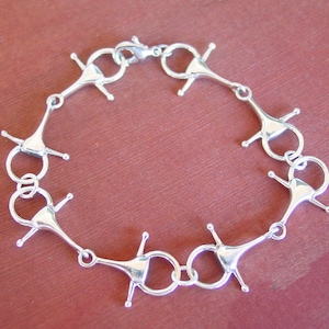 May include: A silver bracelet made of a series of linked, decorative, horse bit-shaped charms.