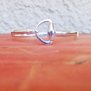 May include: A silver bracelet with a horse bit design. The bracelet is made of metal and has a polished finish.