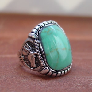 May include: A silver ring with a green turquoise stone and a detailed design on the band.