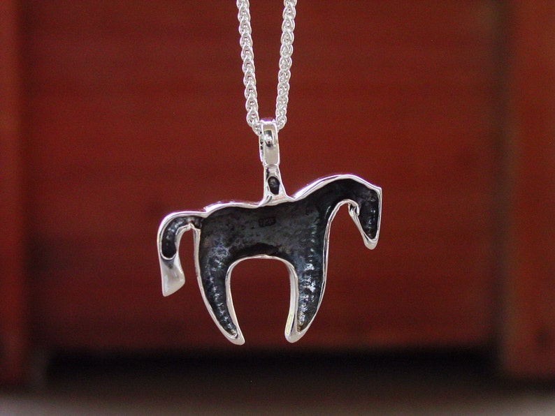 May include: Silver horse pendant necklace. The horse is facing right and has a detailed design. The necklace is on a silver chain.