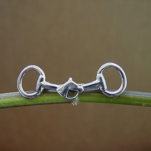 May include: A silver-toned metal horse bit charm, resembling a snaffle bit, is displayed on a green stem.
