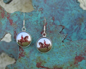May include: A pair of silver earrings with round, white porcelain pendants featuring a vintage illustration of a person riding a brown horse.