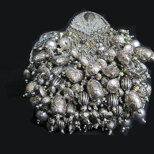 Könnte beinhalten: Eine silberne und graue Perlen-Clutch mit herzförmigem Design. Die Clutch ist mit einer Vielzahl von Perlen bedeckt, darunter runde, ovale und herzförmige Perlen.