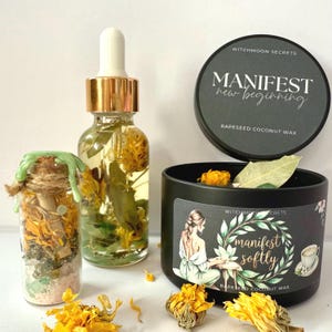 Könnte beinhalten: Eine Auswahl an Selbstpflegeprodukten, darunter eine Glasflasche mit Pipette, ein kleines Glas und eine schwarze Kerze. Auf der Kerze stehen die Worte "manifest softly" und "rapeseed coconut wax". Das Glas ist mit Bindfaden und grünem Wachs versiegelt. Getrocknete Blumen sind verstreut.