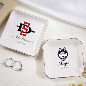 May include: Two white ceramic ring dishes with gold trim. One features a red and black design with the name "Khalani" and "Class of 2026." The other has a husky logo and the name "Aleyna" and "Class of 2026."