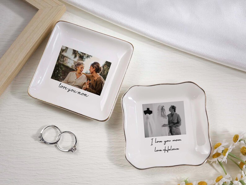 May include: Two white ceramic trinket dishes with gold trim, each featuring a photograph and handwritten text. One says "love you mom", the other says "I love you mom Love Heloise". Silver rings are next to the dishes.