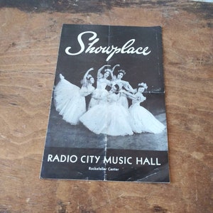 May include: Black and white photo of a group of dancers in white tutus performing on stage at Radio City Music Hall in New York City. The text "Showplace" is at the top of the image and "Radio City Music Hall" is at the bottom of the image.
