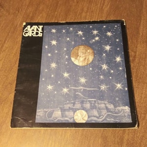 Op de afbeelding: Een vintage platenhoes met een donkerblauwe achtergrond met een wit sterrenpatroon en een zilveren kroon met een gezicht in een cirkel. De albumtitel "AVANT GARDE" is in wit op een zwarte achtergrond gedrukt.