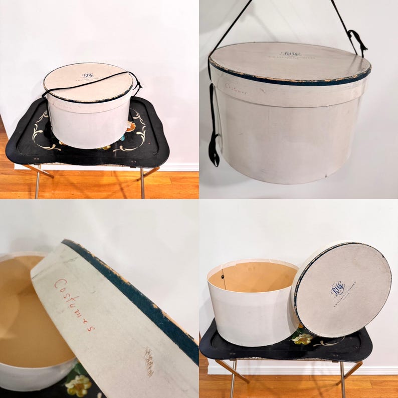 May include: A vintage, off-white hat box with a black handle and trim. The box is cylindrical with a lid and sits on a black tray with gold legs. The lid has the initials "RMC" and the word "Costumes" is printed on the side.
