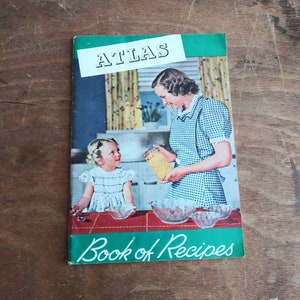 May include: A vintage green and white cookbook with the title "Atlas Book of Recipes". The cover features a woman and a young girl in a kitchen setting, with a jar of preserves and bowls on the counter.