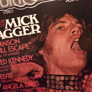Pode incluir: Uma capa de álbum de vinil vintage com Mick Jagger, o vocalista dos Rolling Stones, cantando em um microfone. A capa do álbum é preta com texto branco e apresenta uma foto de Mick Jagger usando um colar preto cravejado.