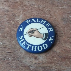 May include: A blue and white round button with the text "PALMER METHOD" and a black and white illustration of a hand holding a pen.