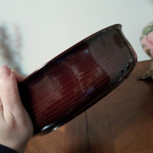 May include: A dark brown wooden bowl with a smooth, glossy finish. The bowl is round and has a slightly curved rim.