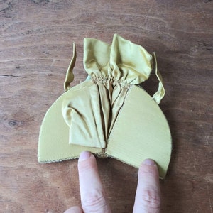 May include: A yellow fabric hat with a gathered top and a wide brim. The hat is folded in half and the inside is visible.