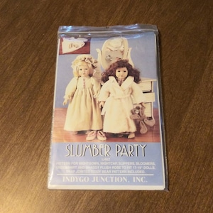 May include: A sewing pattern for a doll slumber party set, featuring a nightgown, nightcap, slippers, bloomers, undershirt, and a shaggy plush robe. The pattern is for 17-19 inch dolls and includes a snap-jointed teddy bear pattern. The pattern is titled "Slumber Party" and is by Indygo Junction, Inc.