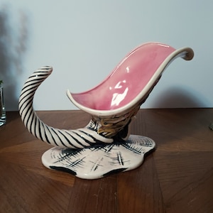 May include: A ceramic cornucopia vase with a pink interior, black and white striped handle, and a gold and black base.
