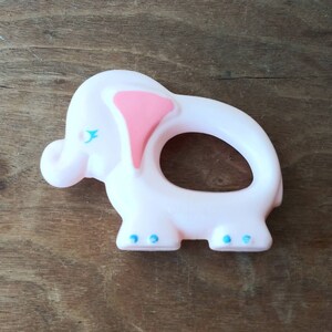 May include: A pink plastic elephant teether with blue eyes and a pink ear. The teether has a ring in the middle for a baby to hold.