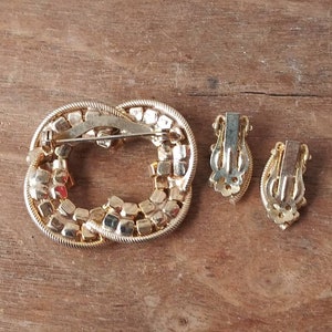 May include: A gold-tone brooch and matching clip-on earrings set with clear and red rhinestones. The brooch is shaped like a knot and the earrings are oval.