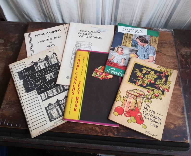 May include: A collection of vintage home canning books with colorful covers and titles like "Home Canning of Fruits and Vegetables", "The Home Canners Text Book", and "The Home Canners Year Book 1929".