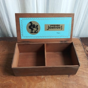 May include: A wooden box with a hinged lid. The lid has a blue and gold label with the text "Howard Johnson's" and a silhouette of a woman carrying a child. The box is divided into two compartments and has the text "Distributed by Henry Limmer No. 1" on the bottom.