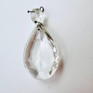 May include: A clear glass crystal teardrop pendant with a faceted design. The pendant is attached to a metal loop.