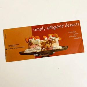 以下が含まれることがあります： 茶色の背景に白い文字で「simply elegant desserts」と書かれた、ビンテージの料理本の表紙。表紙には、ガラスの皿に載せられた3つのアイスクリームデザートの写真が写っている。左下の隅には、「Tested Recipes From the Kitchen of american dairy association」という文字が書かれている。