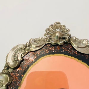 May include: A silver-toned ornate frame with a black and orange glitter background and a pink interior. The frame has a decorative design with a scalloped top.