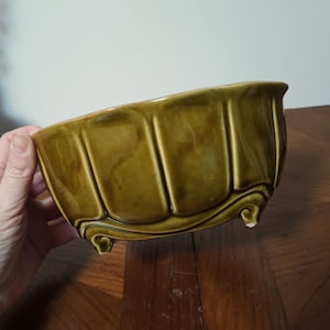 Può includere: Un vaso da fiori in ceramica verde con un design scanalato e tre piedi. Il vaso è in ceramica smaltata e ha una finitura lucida.