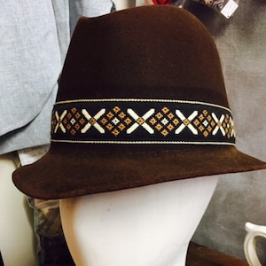 May include: A brown felt fedora hat with a black and brown patterned band. The hat has a wide brim and a slightly indented crown.
