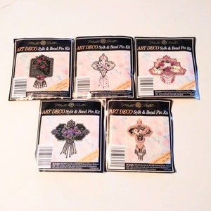 May include: Five packages of Mille Fille Art Deco Sylk & Bead Pin Kits. Each package features a different design of a beaded pin with a floral motif. The pins are in shades of pink, purple, and black.